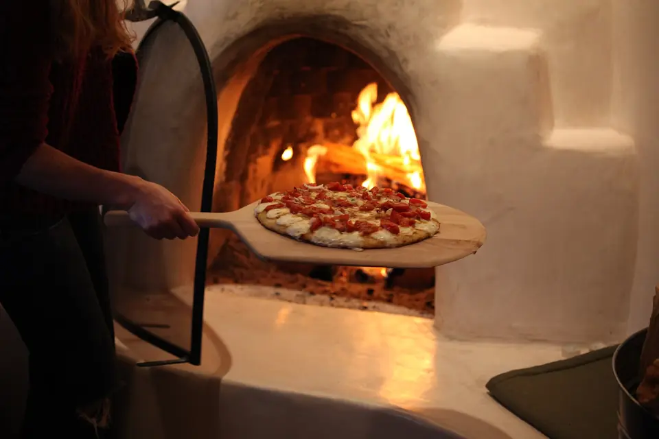 Pizza being pulled from a glowing wood-fired oven